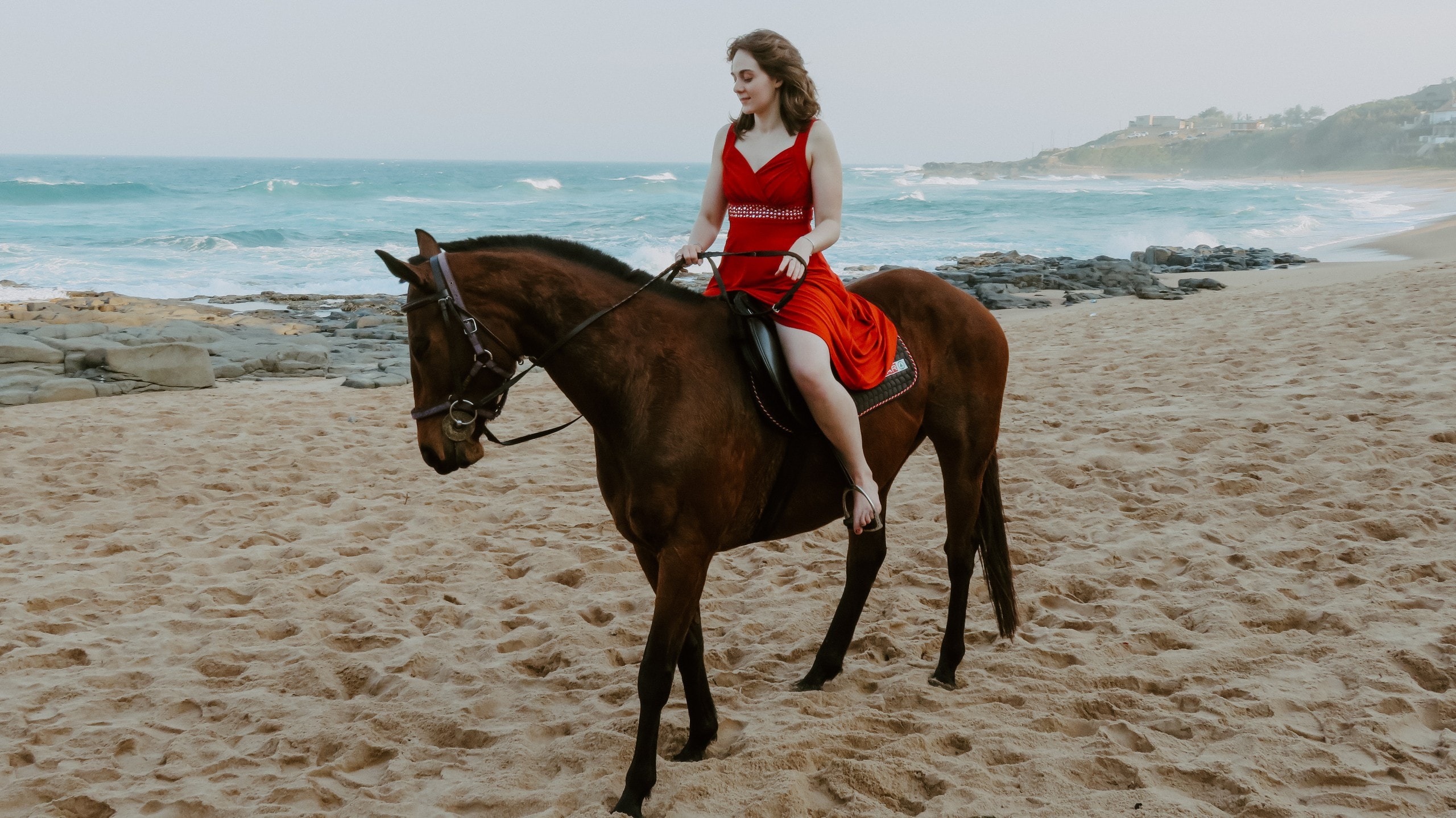 Rider in a red dress on a bay horse along the beach
