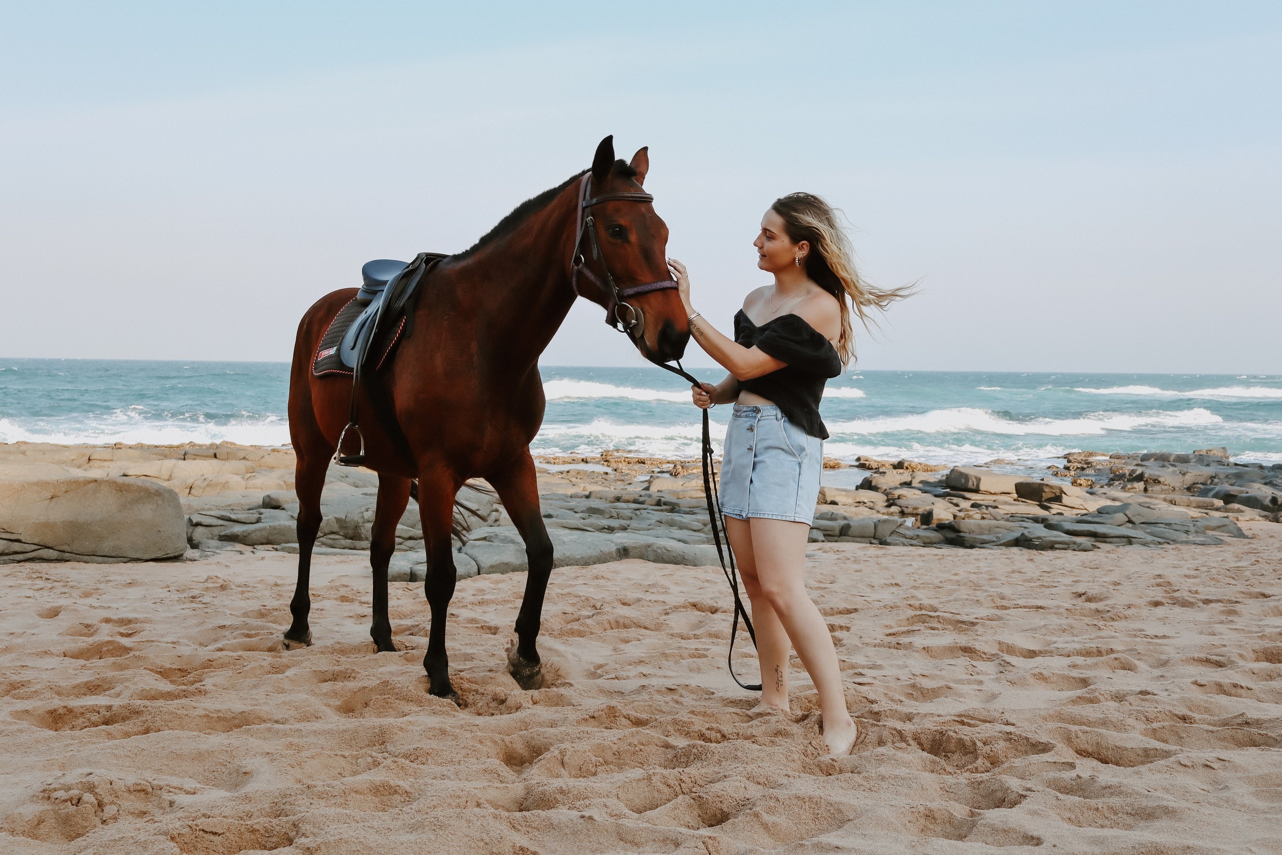 Guest with a saddled horse on sand by the ocean