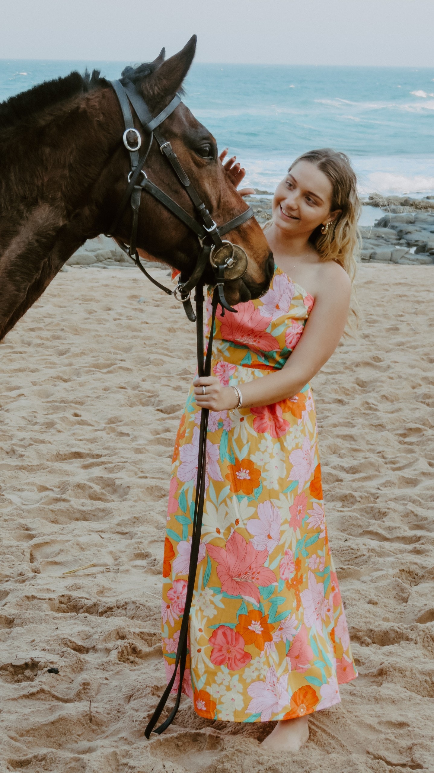 Guest in a floral dress standing with a horse on the beach